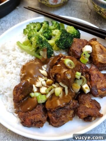 Satay chicken with rice and broccoli covered with satay sauce on a white plate with chopsticks.
