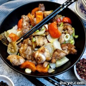 A black serving dish containing salt and pepper chicken. There are black chopsticks in the dish.