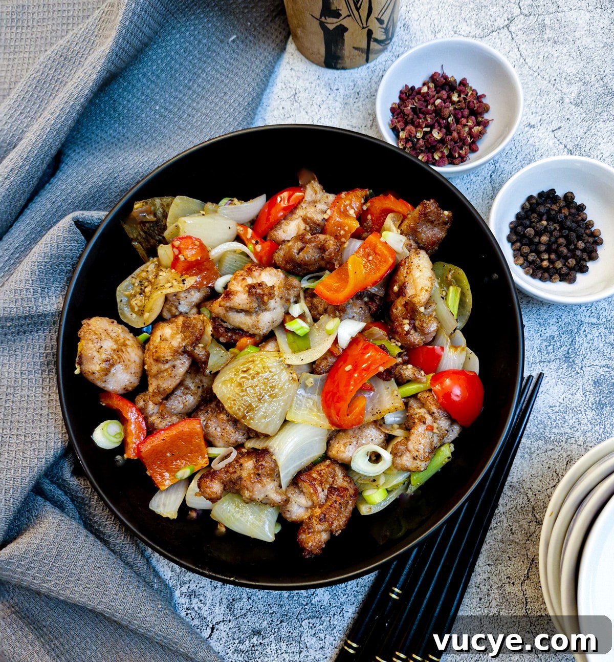 Crispy Salt and Pepper Chicken Recipe for Dinner 3 Overhead shot of a black serving dish of salt and pepper chicken with 2 small white dishes of peppercorns on the table.
