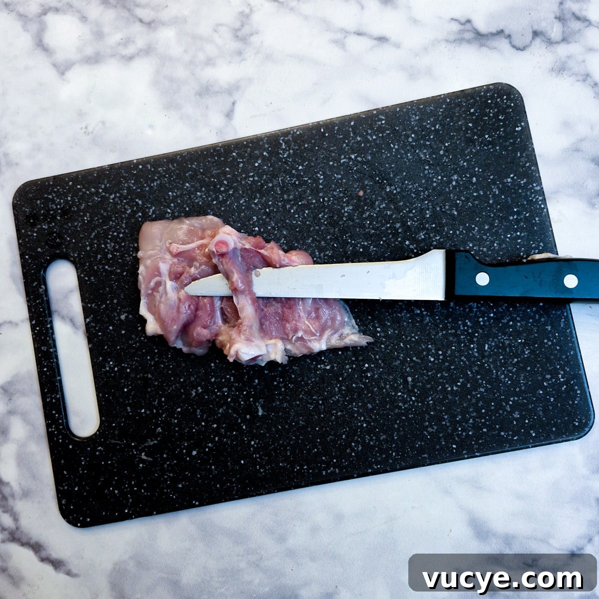Crispy Salt and Pepper Chicken Recipe for Dinner 5 A raw chicken thigh with the meat cut away from the thigh bone and a sharp knife inserted between the bone and the meat.