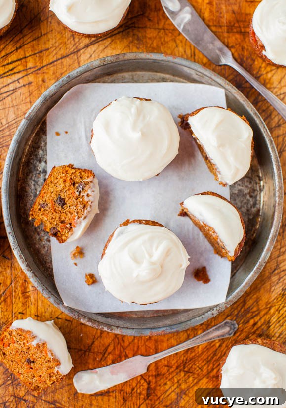 Carrot Cake Cupcakes with Vanilla Cream Cheese Frosting Recipe 3 A tray of carrot cake cupcakes with cream cheese frosting, one cut in half to show the inside.