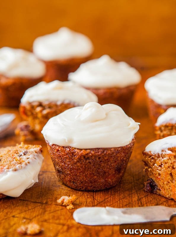 Carrot Cake Cupcakes with Vanilla Cream Cheese Frosting Recipe 4 A selection of freshly baked carrot cupcakes topped with cream cheese frosting, with one partially eaten on a wooden surface.