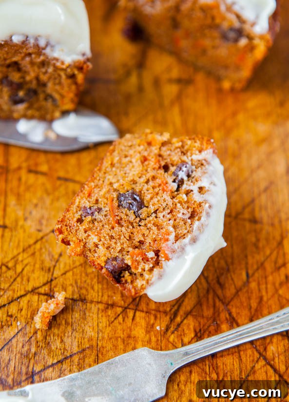 Carrot Cake Cupcakes with Vanilla Cream Cheese Frosting Recipe 5 A slice of carrot cake with cream cheese frosting on a wooden surface with a fork.