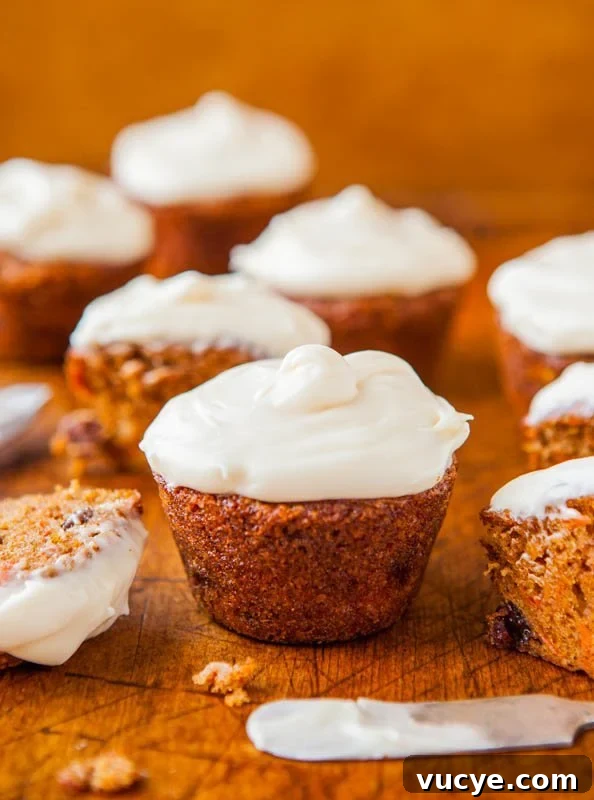 Carrot Cake Cupcakes with Vanilla Cream Cheese Frosting Recipe 6 A selection of freshly baked carrot cupcakes topped with cream cheese frosting, with one partially eaten on a wooden surface.