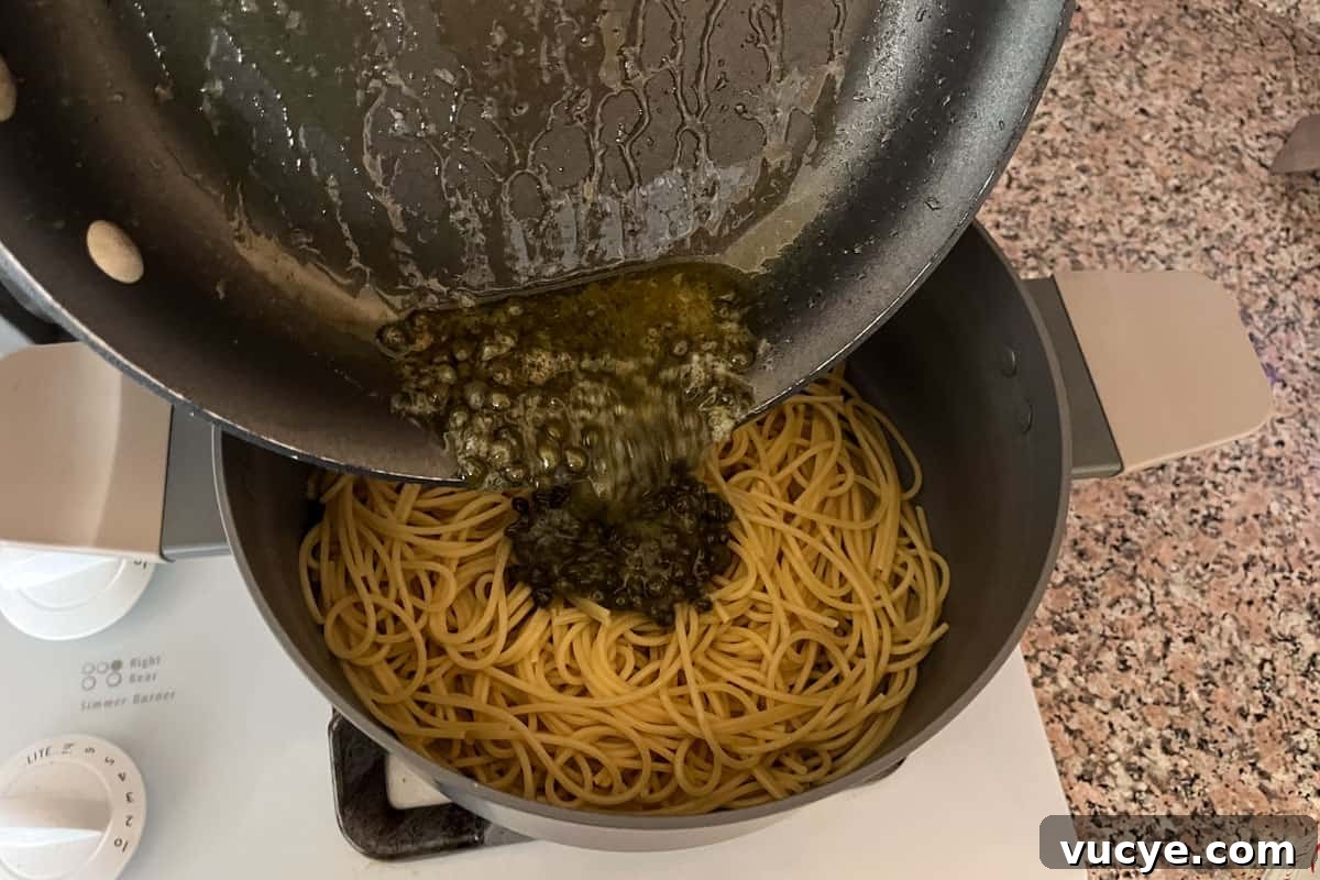 Zesty Lemon Caper Pasta with Garlic and Parmesan 6 Lemon caper sauce being poured from a skillet into a pot of spaghetti.