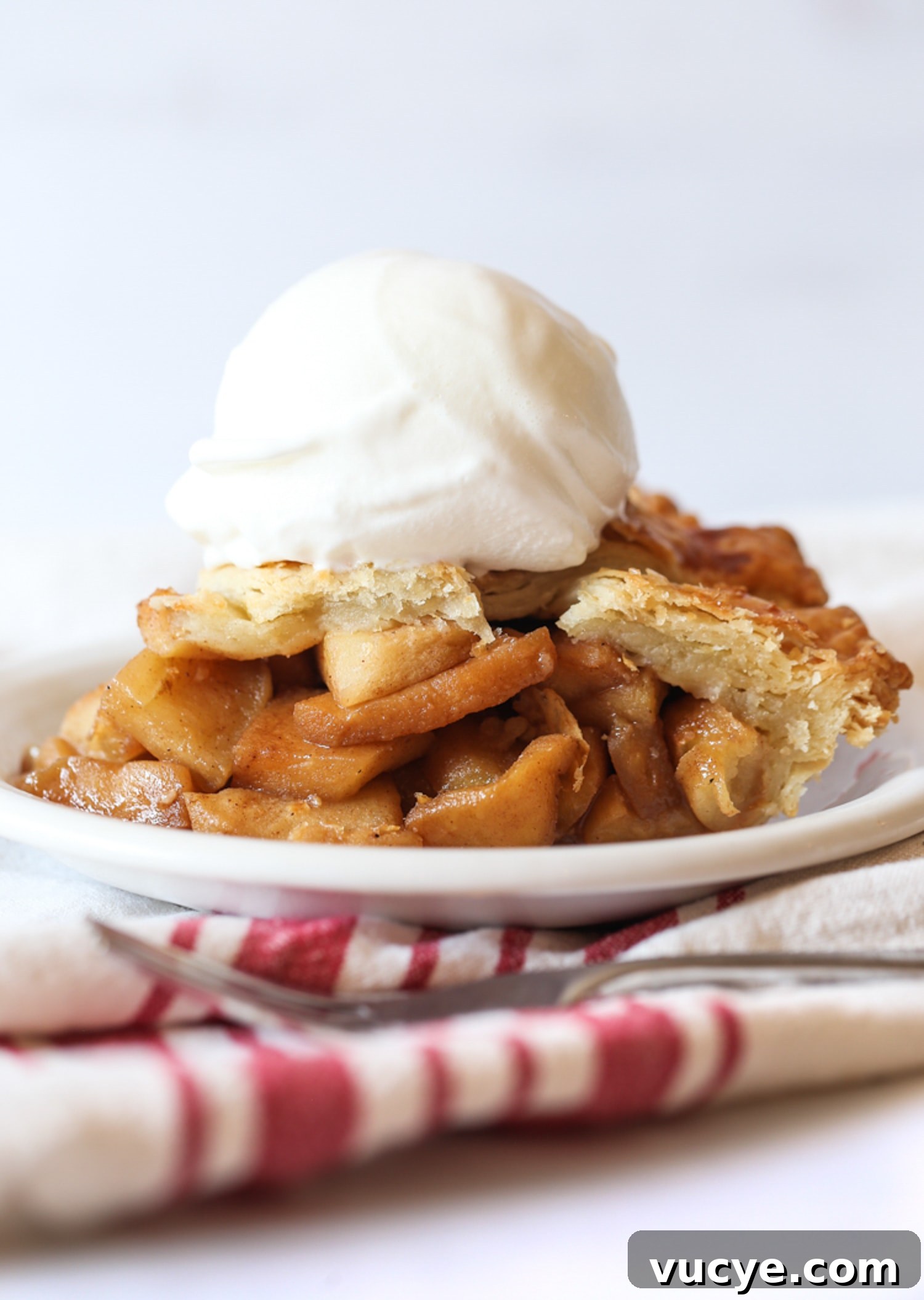 This easy Apple Pie recipe truly makes the best homemade pie! It's a flaky, buttery pie crust loaded with cinnamon-sugar caramelized apples. A slice of apple pie on a white plate with a scoop of vanilla ice cream on top