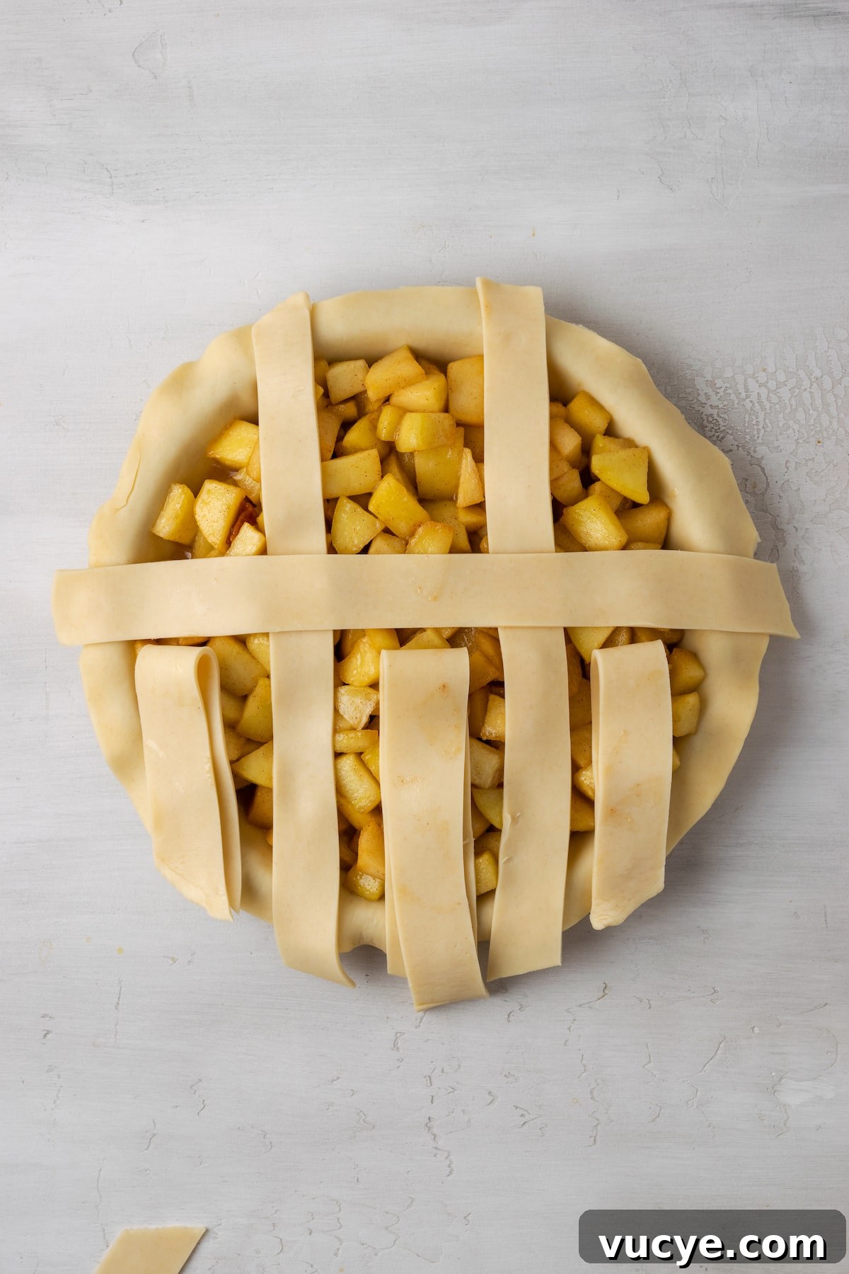 Lay a strip horizontally. An apple pie with a partially completed lattice top.