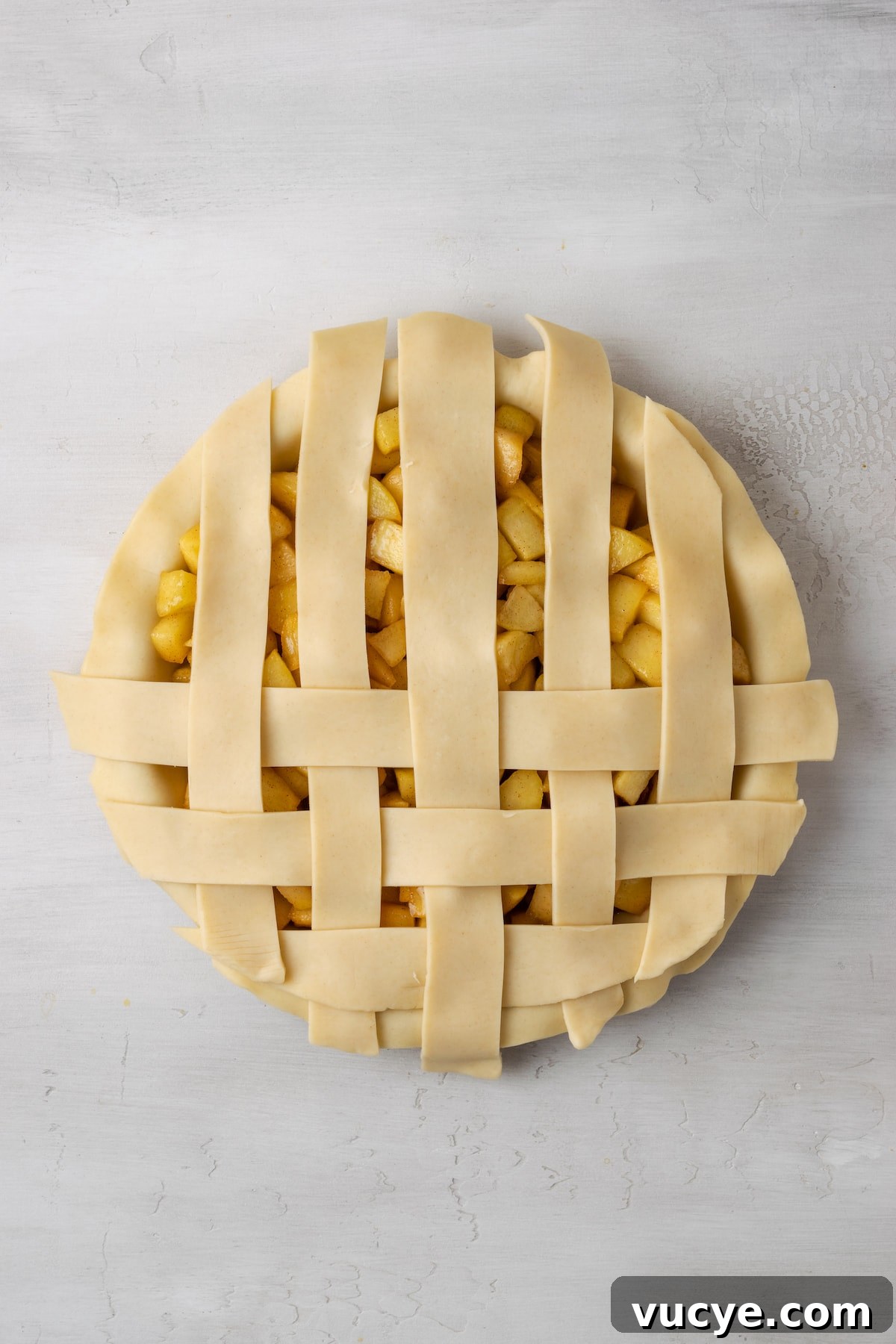 Unfold the strips. An apple pie with a partially completed lattice top.