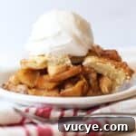A slice of homemade apple pie on a white plate topped with a scoop of vanilla ice cream.