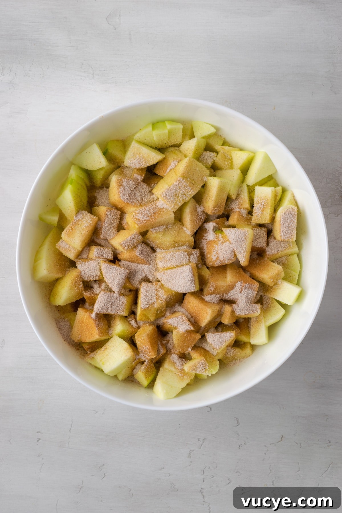 Mix the apples and cinnamon sugar. Apple slices covered with cinnamon sugar in a large white bowl.