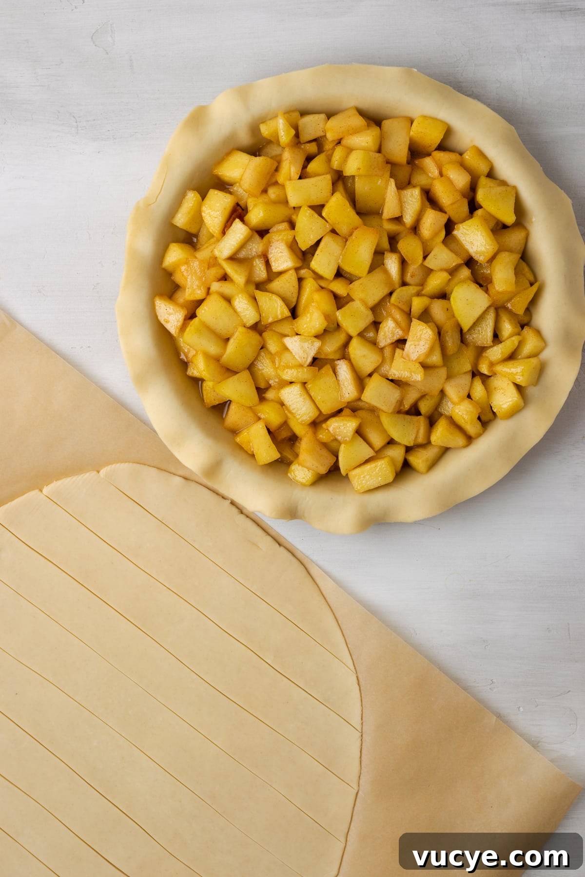 Cut it. A filled apple pie crust next to a second pie crust cut into strips on a piece of parchment paper.