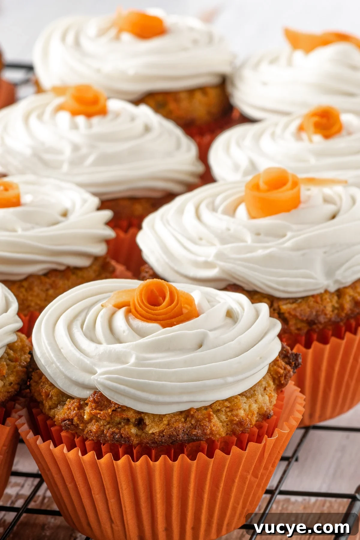 Low-Carb Carrot Cake Muffins with Cream Cheese Frosting 2 Close up of a batch of low carb carrot cake muffins with swirls of cream cheese frosting and small orange roses on the top.