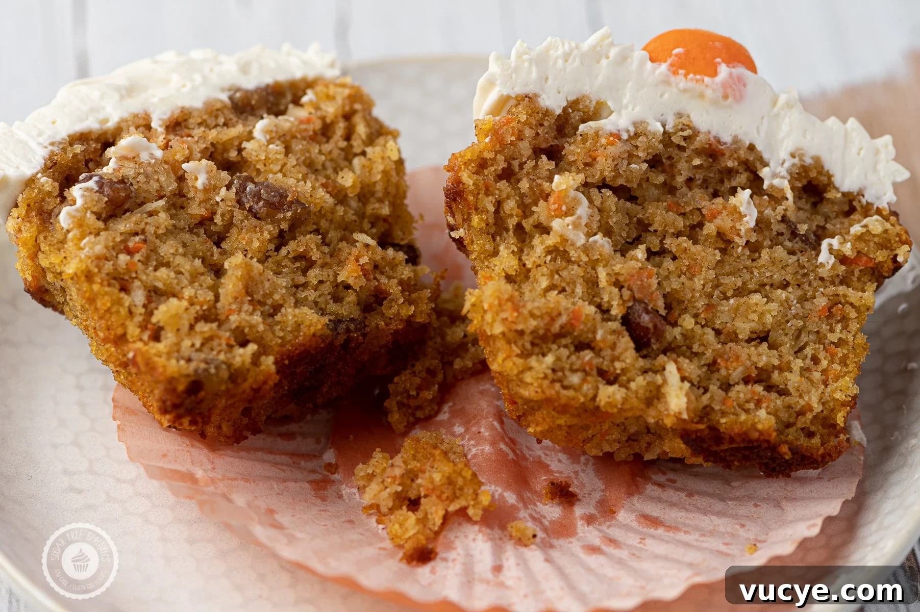 Low-Carb Carrot Cake Muffins with Cream Cheese Frosting 8 A carrot cake muffin with cream cheese frosting cut down the center and place on a white textured plate.