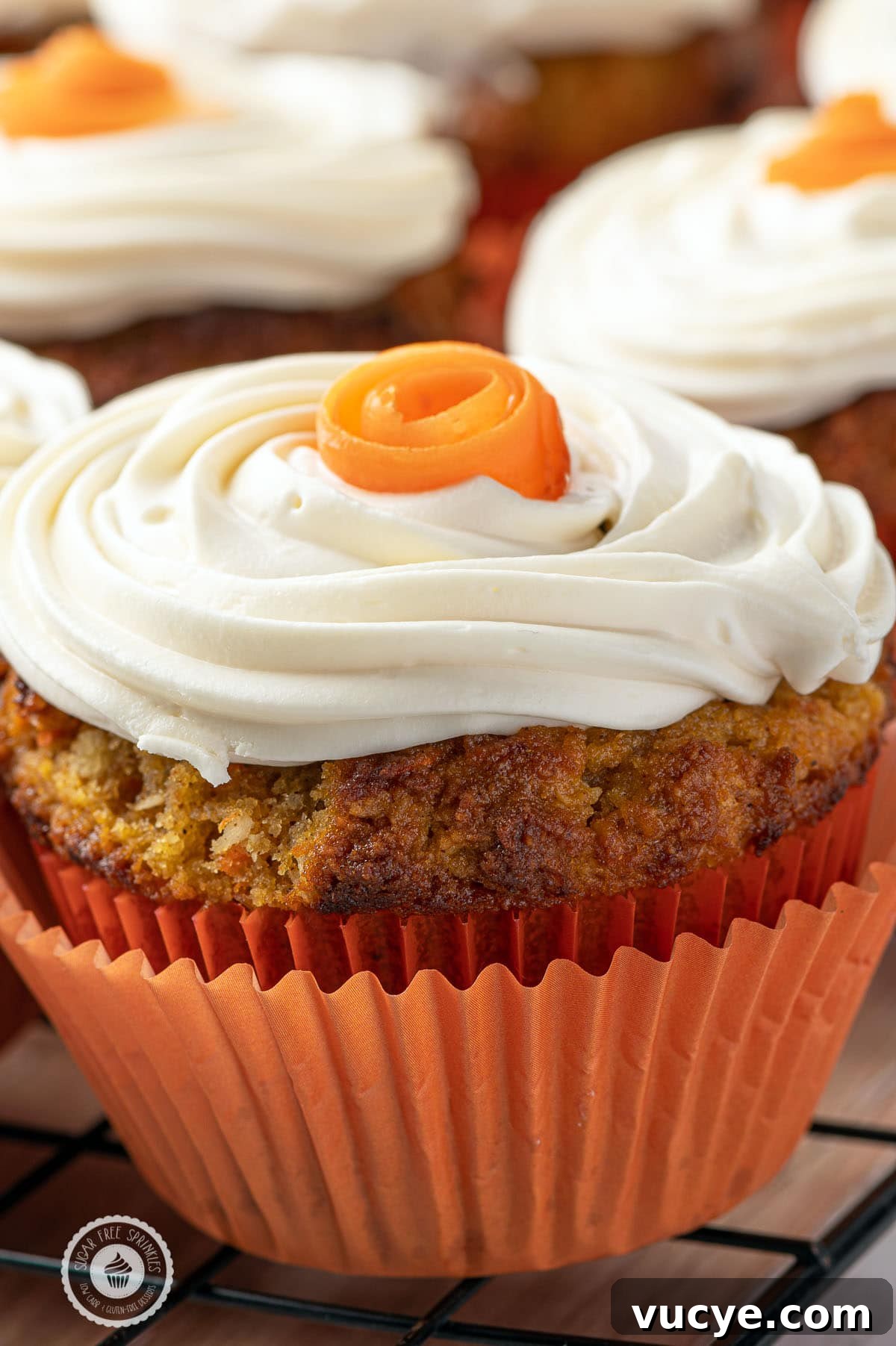 Low-Carb Carrot Cake Muffins with Cream Cheese Frosting 3 Close up of a low carb carrot cake muffins in an orange muffin rapper with swirls of cream cheese frosting and small orange roses on the top.