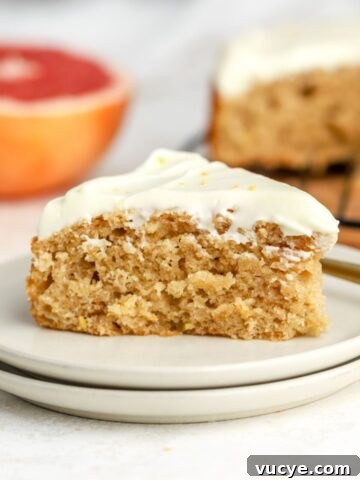 A slice of cake on a plate next to a grapefruit.