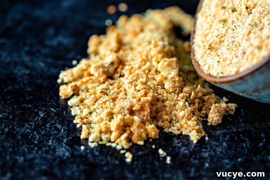 Crispy Puff Pastry Cheese Straws Recipe 4 A close-up of grated Parmesan cheese mixed with spices tipping out of a small bowl and onto a black surface.