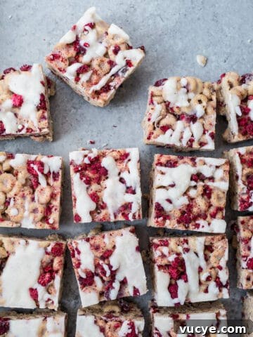 Cereal treats with raspberries and icing on a blue surface.