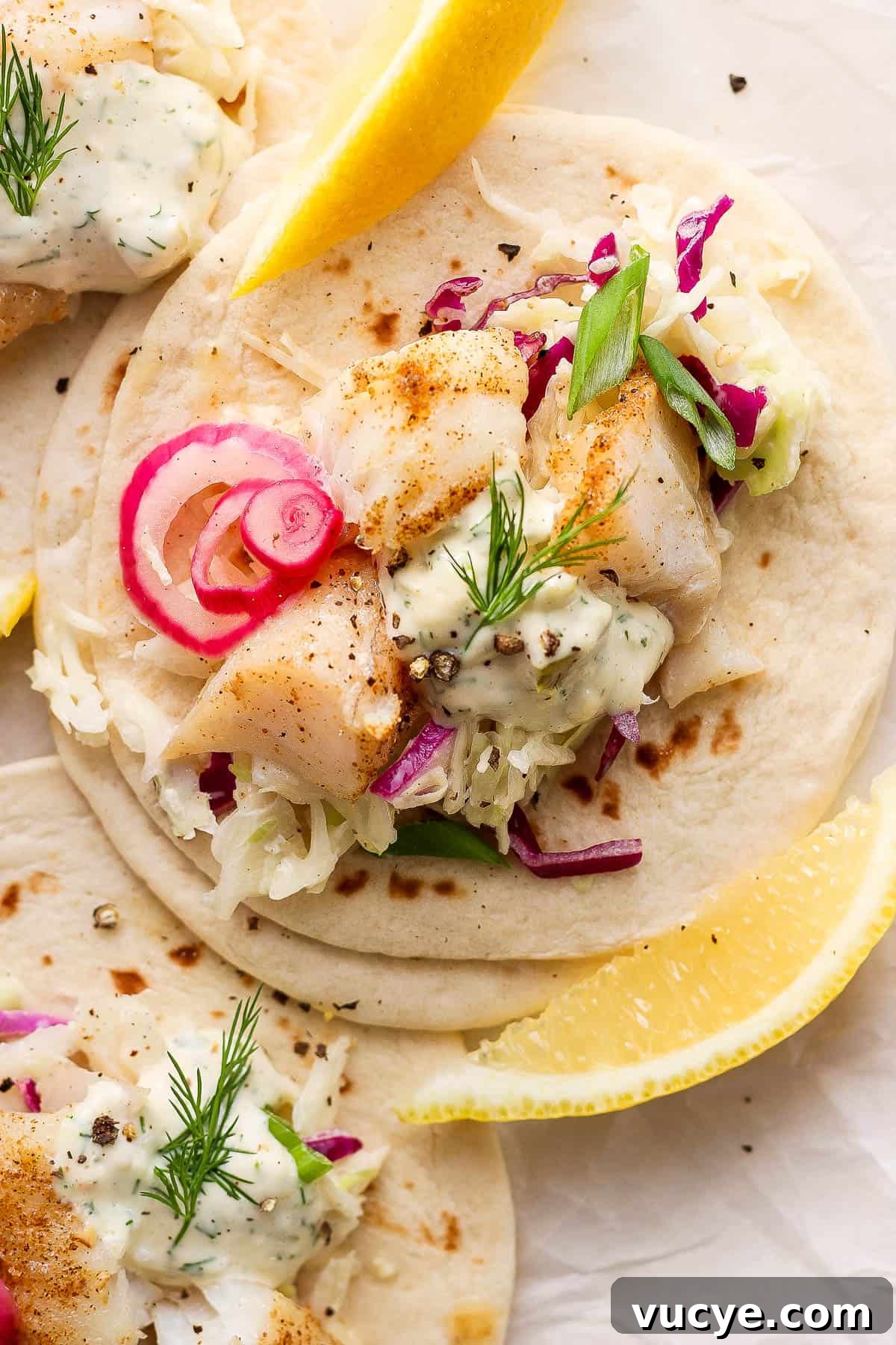 Crispy Cod Tacos with Zesty Slaw and Lime Crema 2 Cod taco topped with creamy slaw, pickled red onion, all on a flour tortilla.