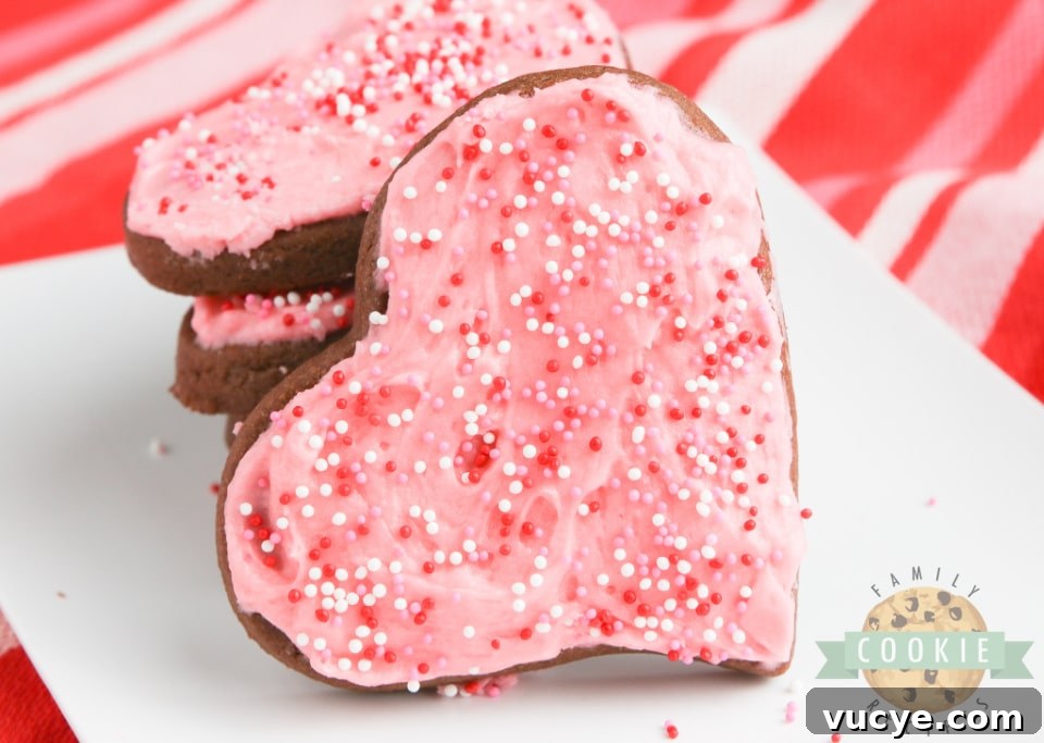 Chocolate sugar cookies cut into heart shapes with pink frosting and sprinkles.