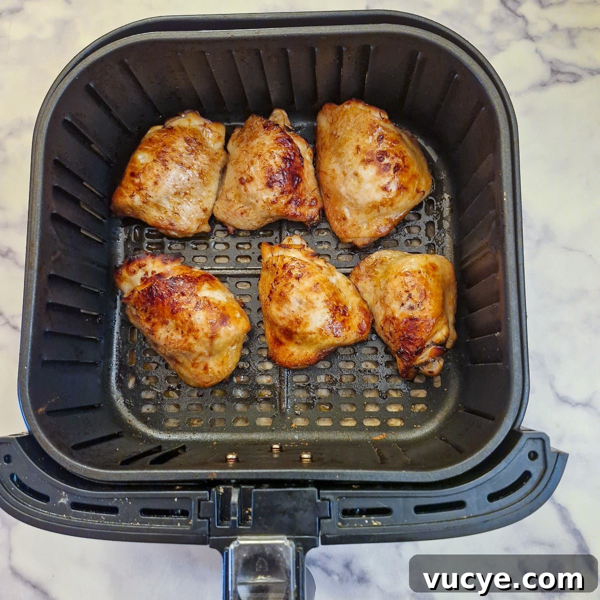 Completely browned chicken thighs in an air fryer basket.