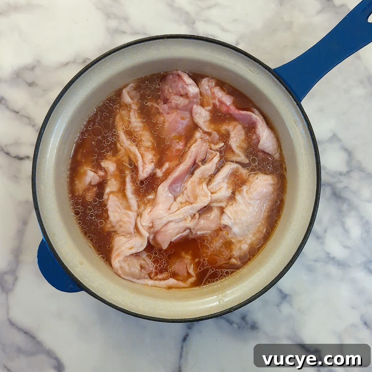 Pieces of chicken combined with marinade in a saucepan.