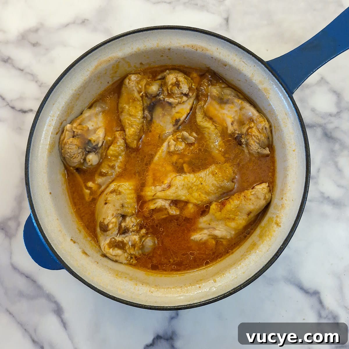 Chicken thighs that have been par-boiled in marinade in a saucepan.
