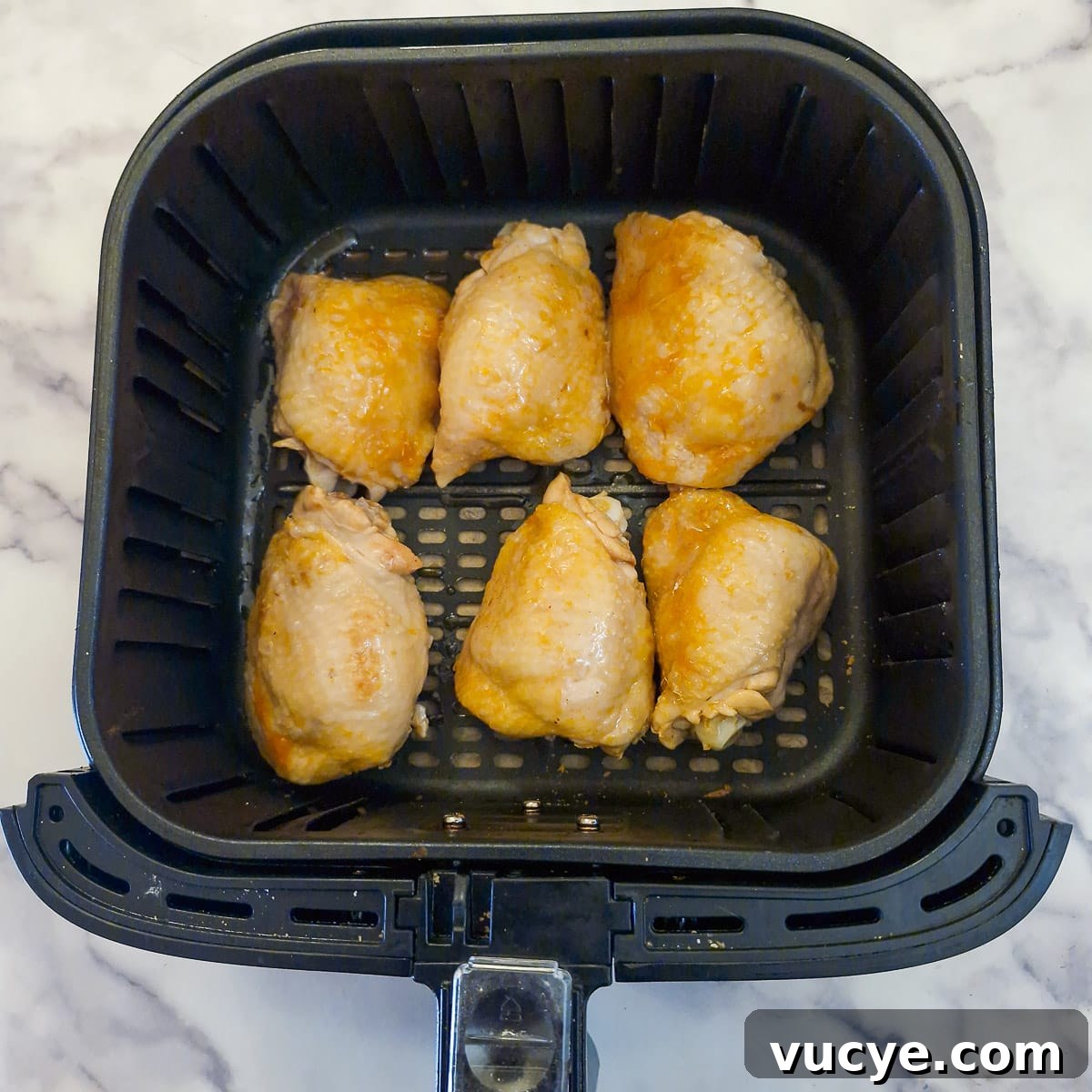 6 chicken thighs, skin side up, in an air fryer basket.