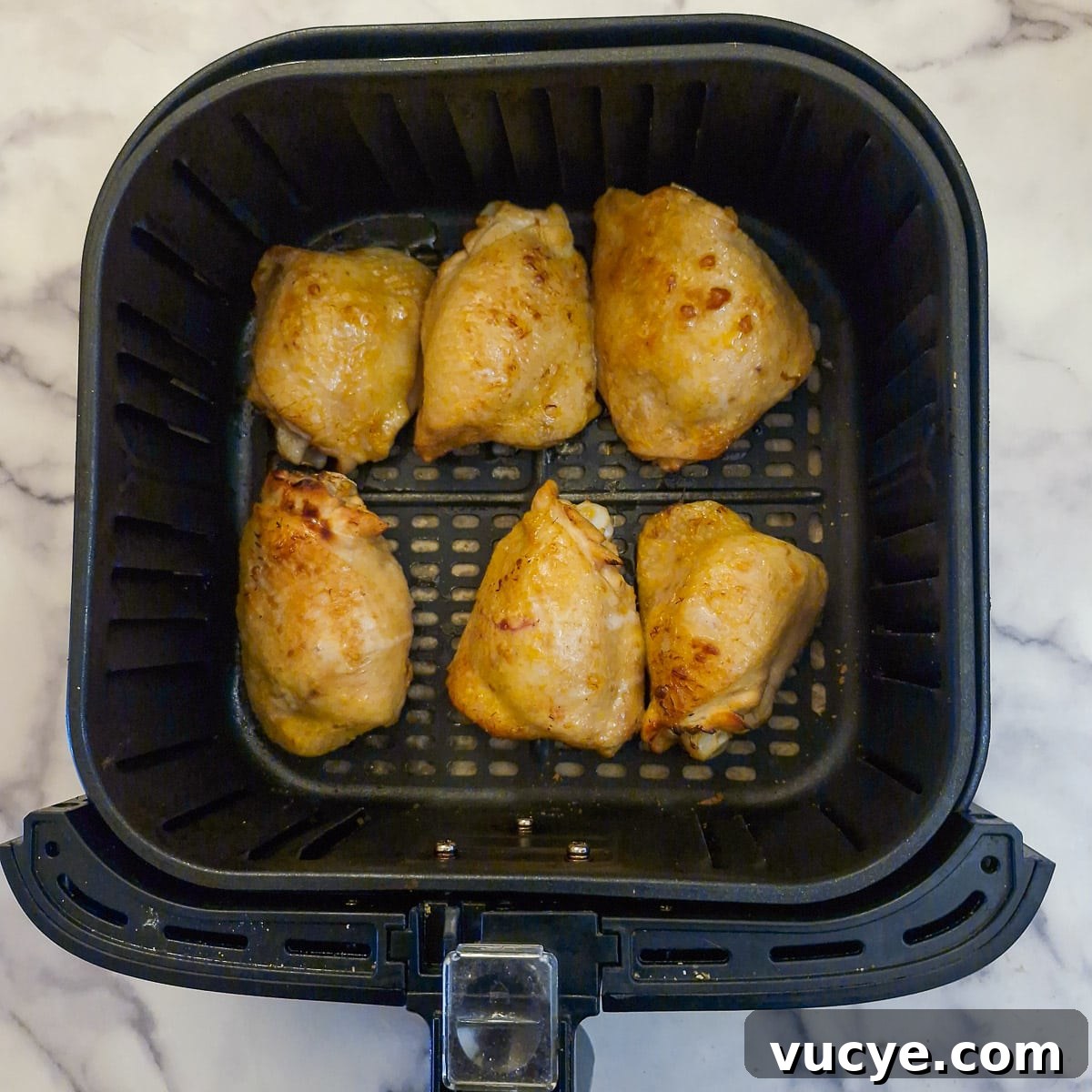 Half-browned chicken thighs in an air fryer basket.