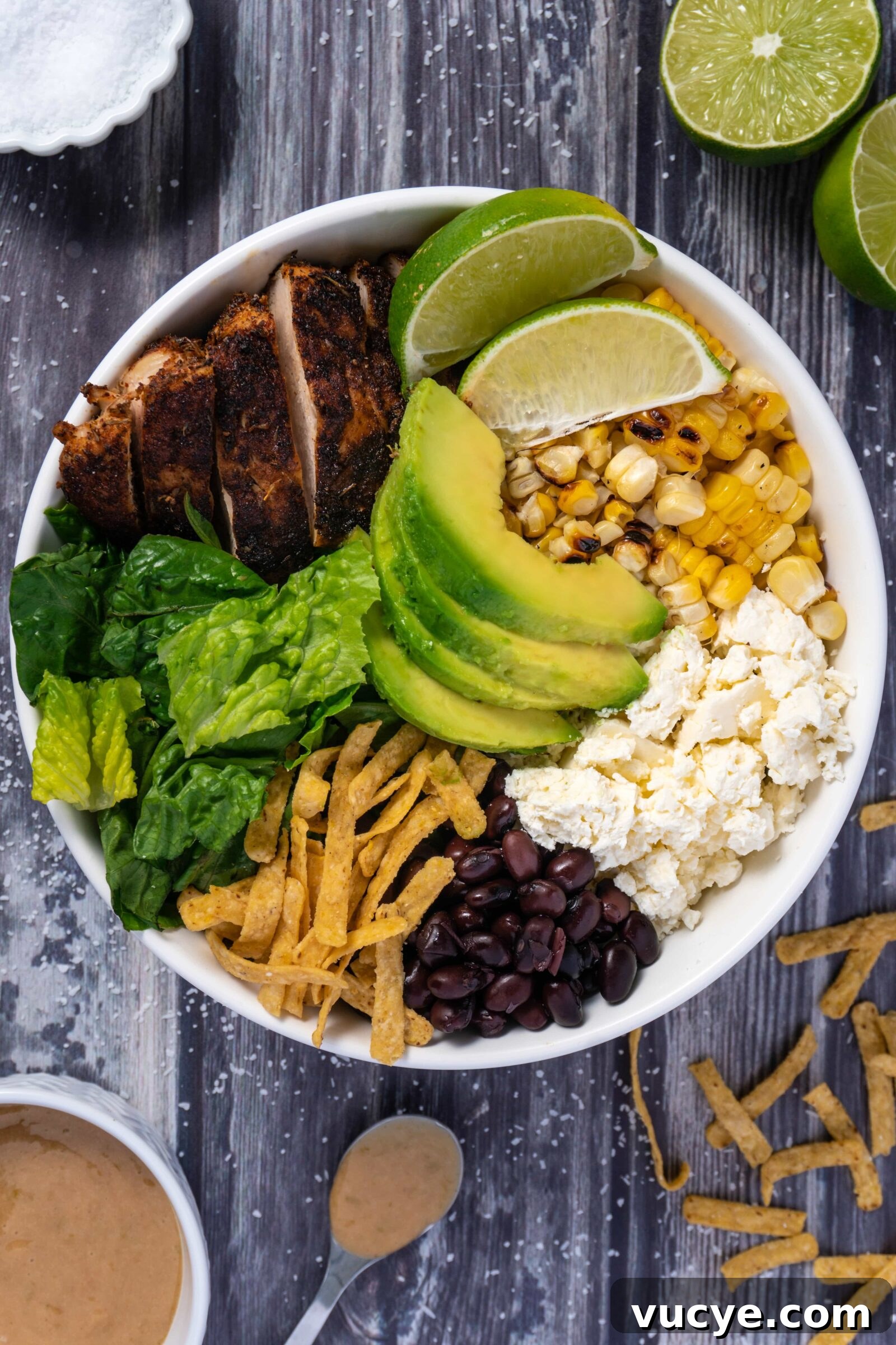 Cajun chicken, romaine lettuce, corn. feta, black beans, dates, tortilla strips, avocado, and limes are added into a bowl and tossed with peanut lime vinaigrette