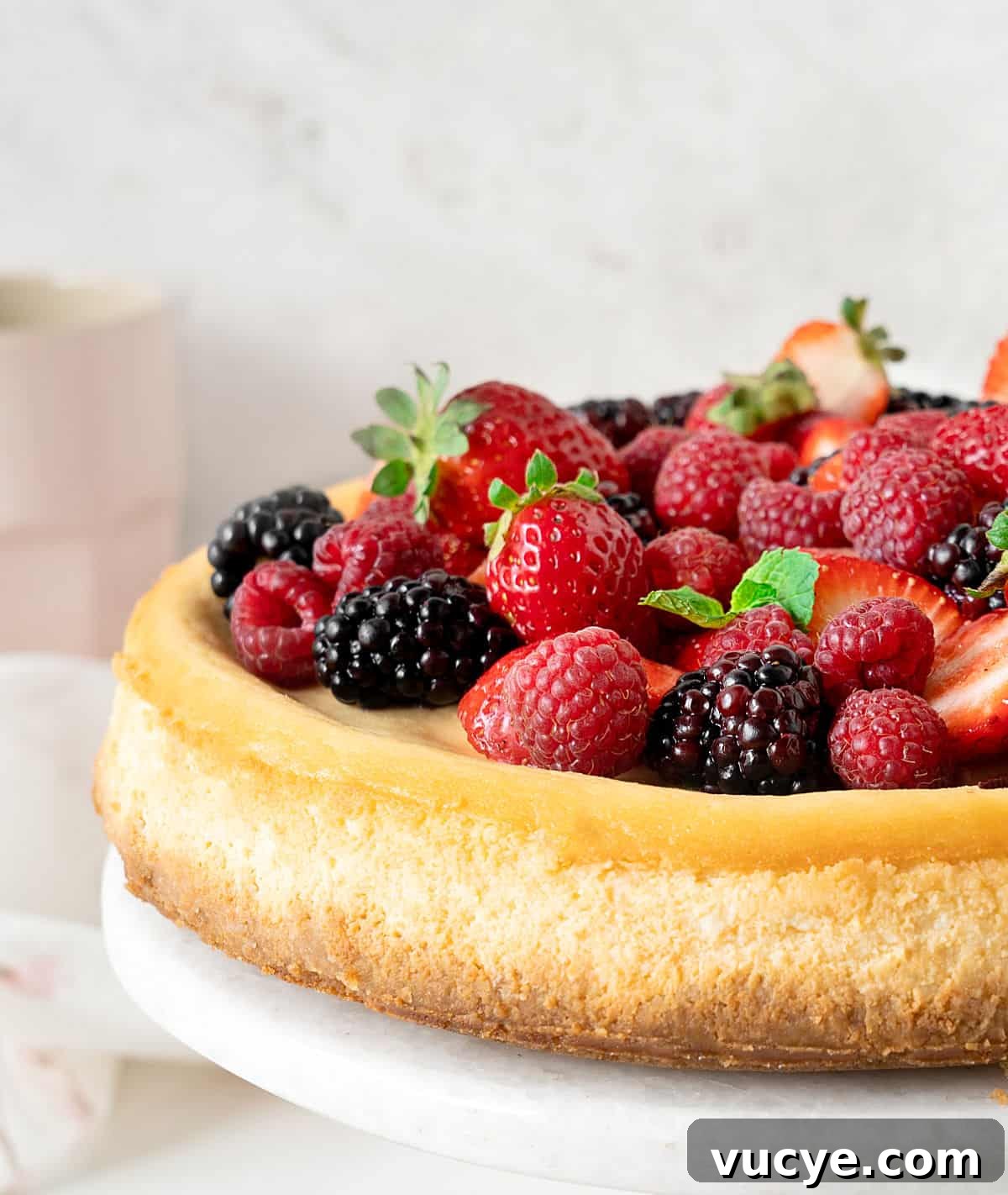 Silky Ricotta Cheesecake Recipe for a Light, Creamy Dessert 2 Partial view of ricotta cheesecake topped with fresh berries on a white marble plate. Light grey background.