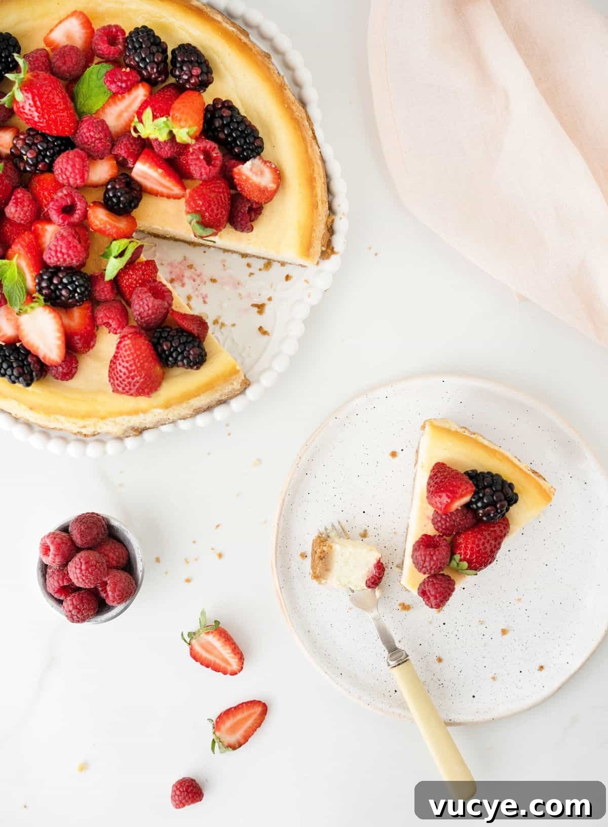 Silky Ricotta Cheesecake Recipe for a Light, Creamy Dessert 11 Top view of ricotta berry cheesecake on a plate with a slice missing that's on a white plate with a fork. White surface.