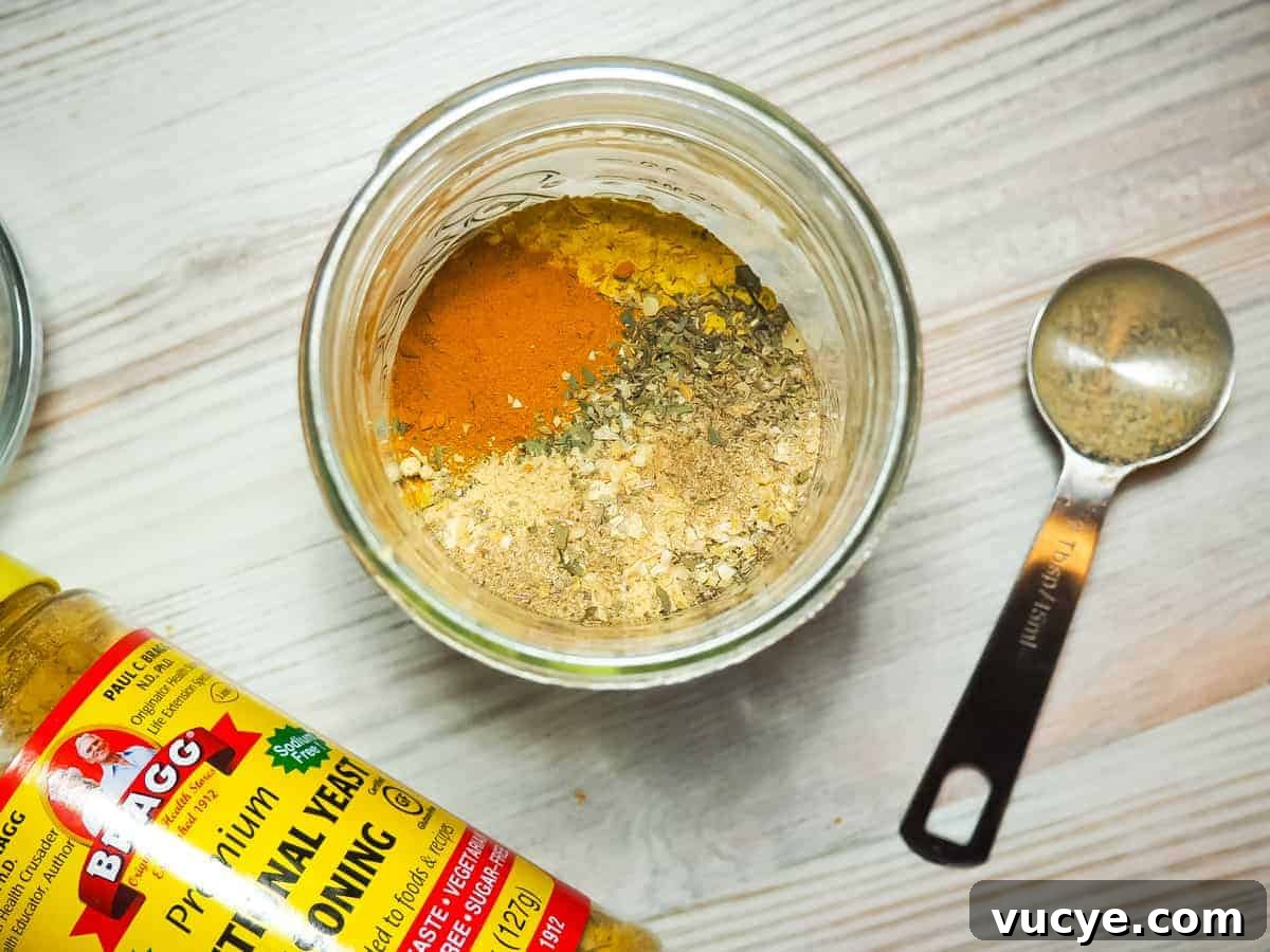 A mason jar full of spices used to make homemade paleo chicken bouillon. Thyme, nutritional yeast, salt, ginger, umami, and oregano.
