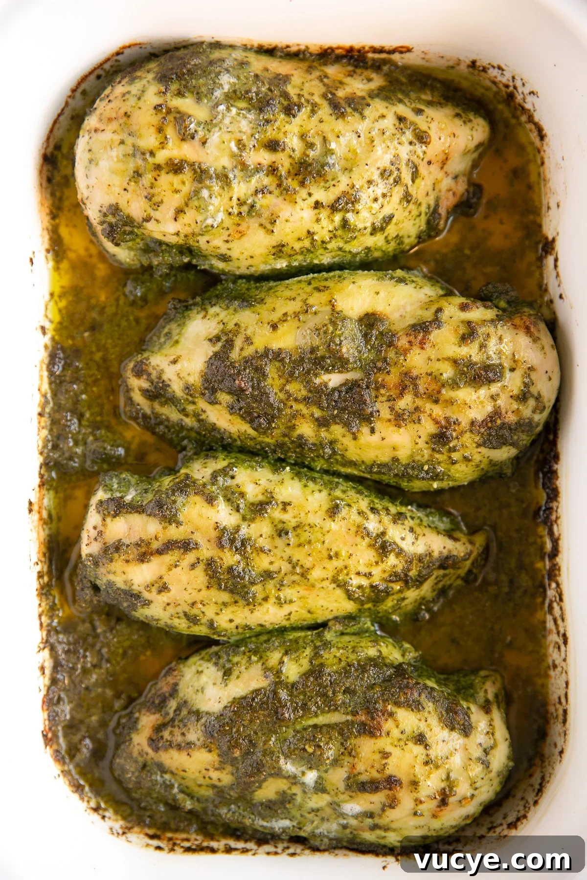 One-Pan Pesto Chicken with Roasted Vegetables 7 White baking dish with four chicken breasts cooked in homemade pesto sauce.