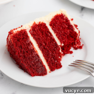 Homemade Red Velvet Cake Recipe From Scratch 18 a slice of layered red velvet cake with cream cheese frosting on a white plate with a fork leaning on it