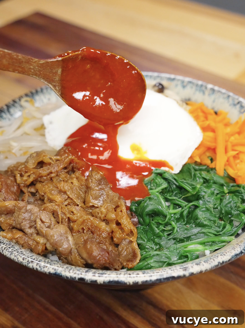 Authentic Beef Bibimbap Recipe with Crispy Veggies and Gochujang 7 Spoon pouring gochujang sauce over rice beef and vegetables in a bowl for beef bibimbap recipe.