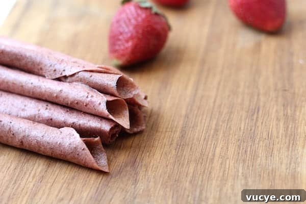 Strawberry Banana Fruit Leather Recipe for Homemade Snacks 3 Photo shows a pile of fruit leather on a table next to strawberries