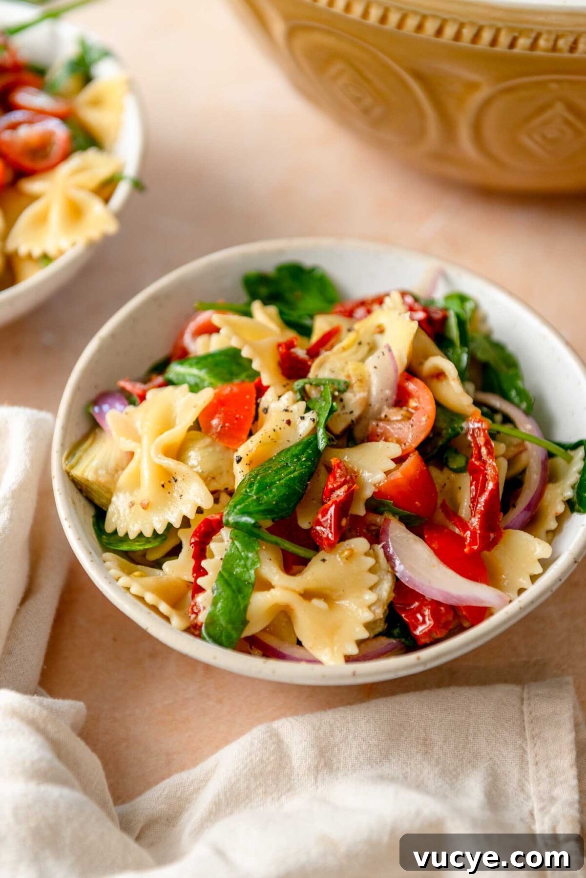 Bowl of sun dried tomato pasta salad with spinach, red onion and artichokes.