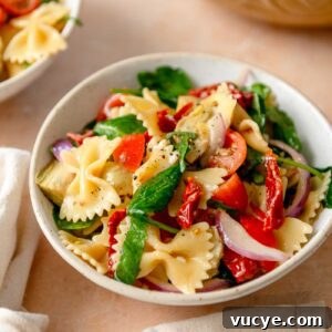 Bowl of sun dried tomato pasta salad with spinach, red onion and artichokes.