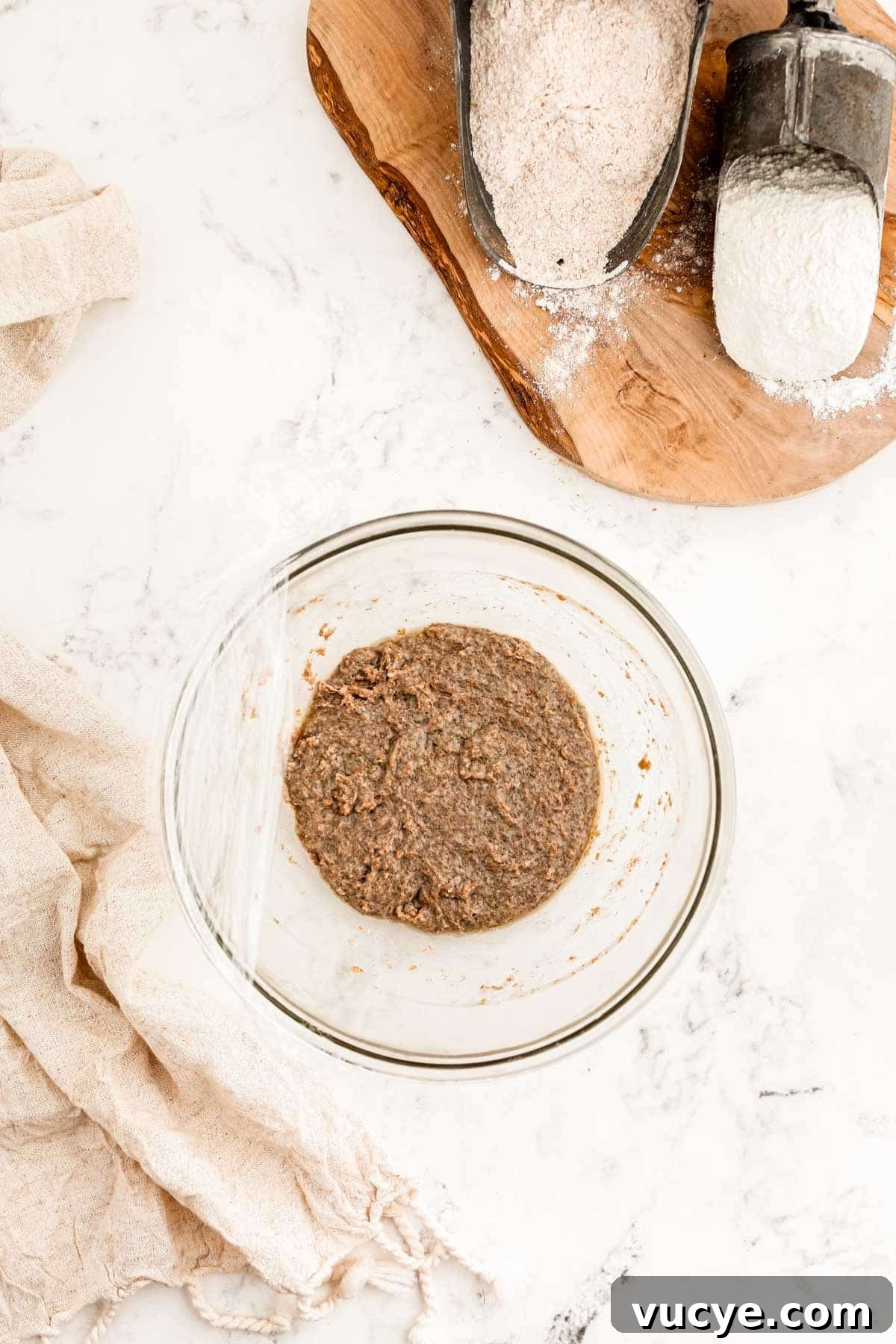 Create a Sourdough Starter at Home: Step-by-Step Guide 6 The beginnings of a sourdough starter in a bowl being covered with plastic wrap.
