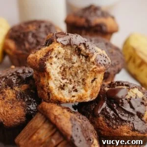 Bakery-Style Chocolate Chunk Banana Muffins Recipe 15 Banana muffins in a pile, one with a bite taken out of it.