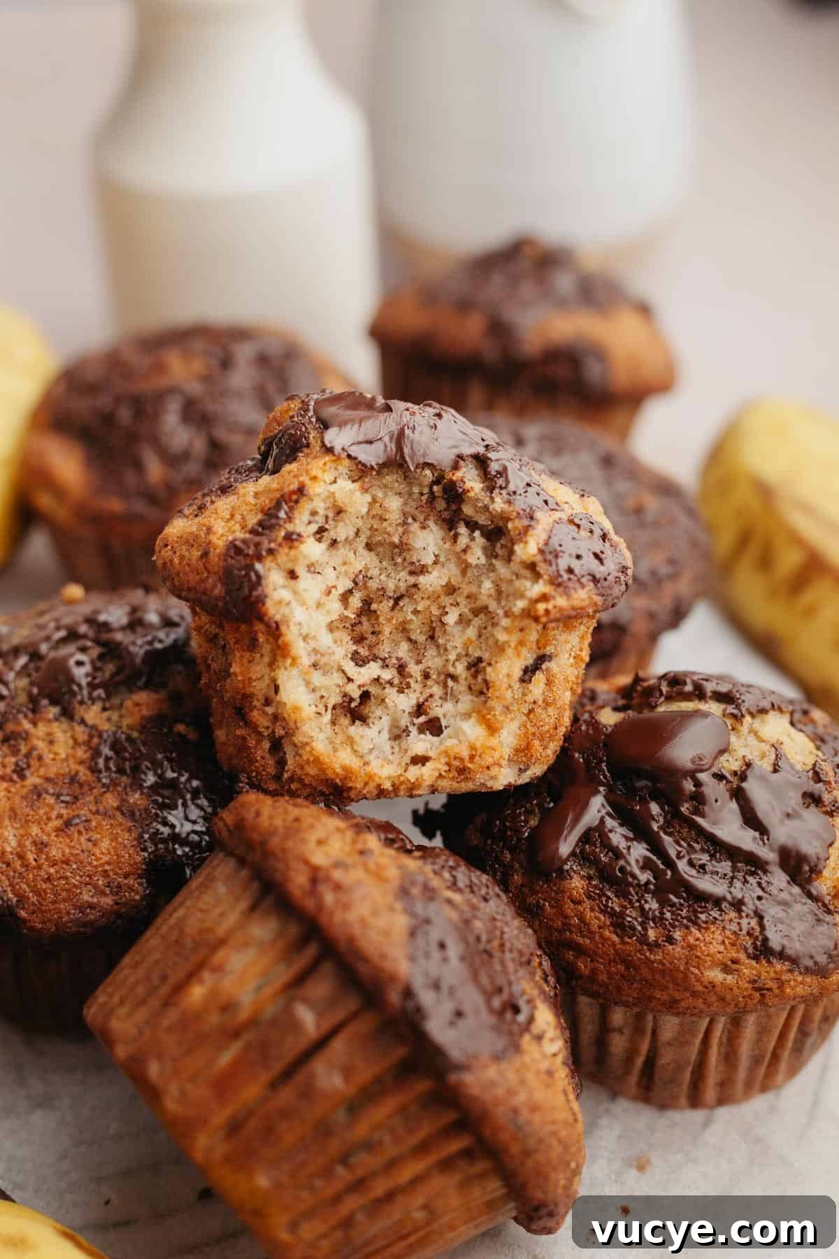 Bakery-Style Chocolate Chunk Banana Muffins Recipe 9 Banana muffins in a pile, one with a bite taken out of it.