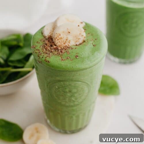 A large glass with a green smoothie in it, topped with banana slices.