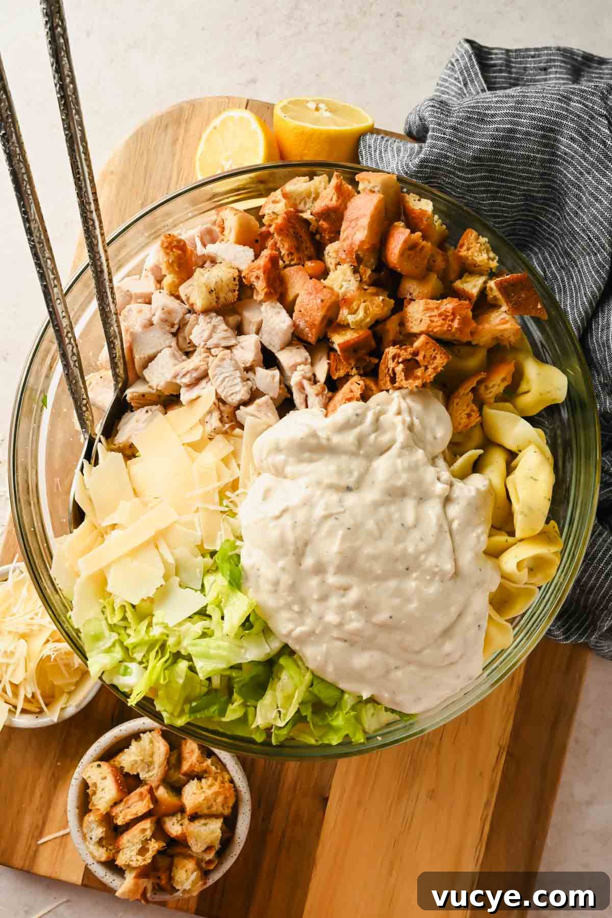 Creamy Caesar Pasta Salad with Crispy Croutons and Parmesan 9 tortellini pasta salad with caesar dressing ingredients with tongs prior to tossing in glass bowl.