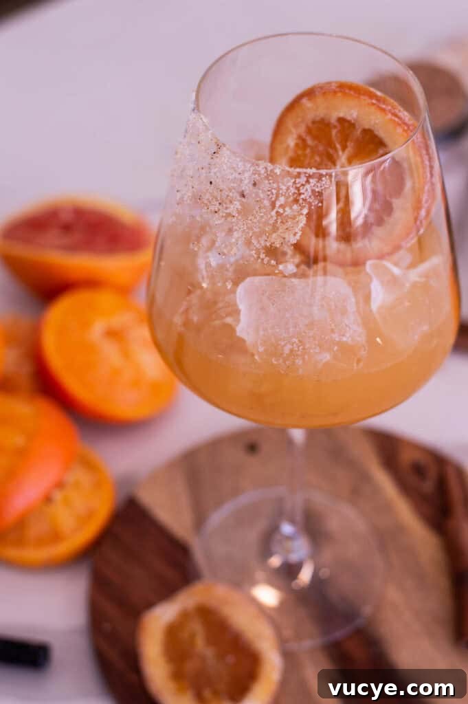 5-Minute Spiced Orange Mocktail — Single-Serve Recipe 5 Glass of orange liquid with a candied orange slice, resting on a wooden cutting board near oranges that are blurred in the background.