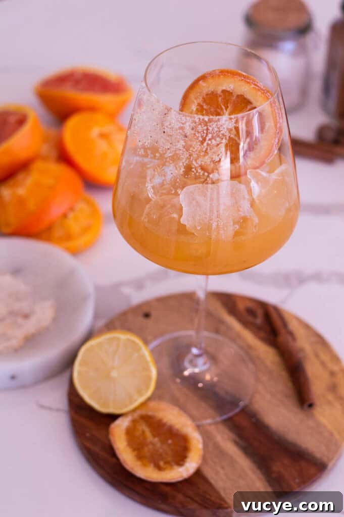 5-Minute Spiced Orange Mocktail — Single-Serve Recipe 6 Glass filled with an orange mocktail and a candied orange slice, resting on a round, wooden cutting board