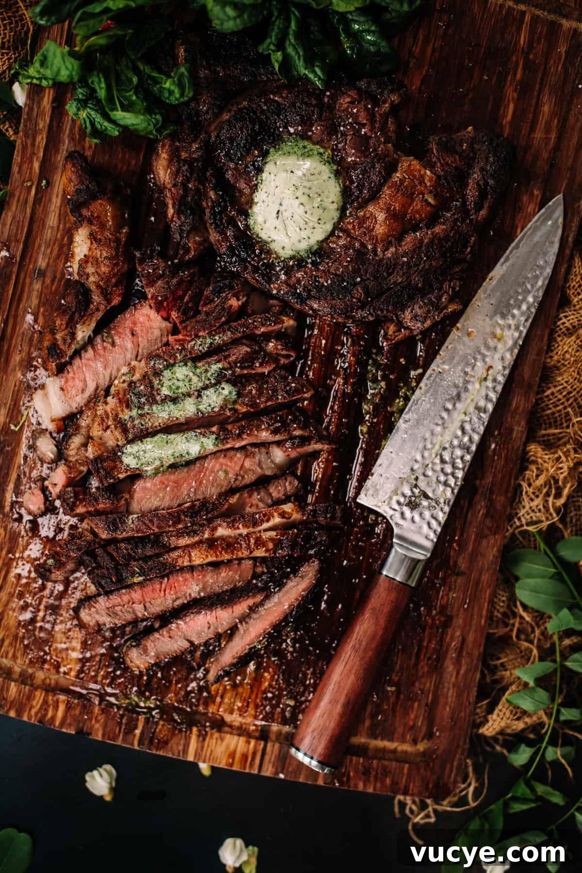 A steak on a cutting board with herbs and a knife.