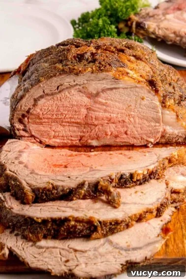 A sliced, seasoned roast beef showing a pink, medium-rare interior on a wooden cutting board with a plate of food and parsley in the background.