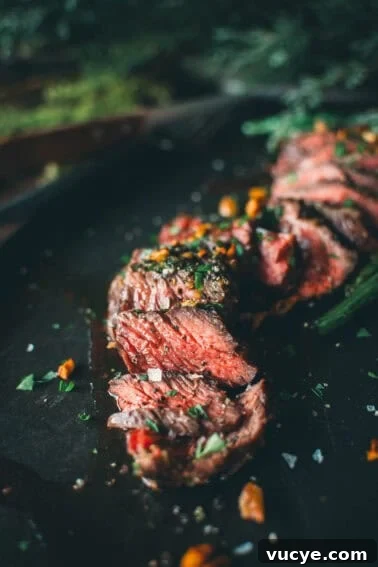 Sliced medium-rare steak garnished with herbs and coarse salt on a dark surface.