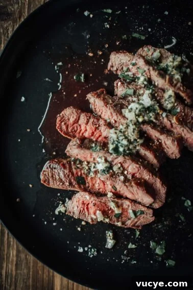 A plate of sliced flat iron steak topped with herbs and seasoning, served on a dark dish.