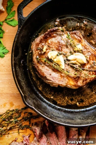 A bone in seared ribeye in a skillet with garlic and butter melted in the drippings